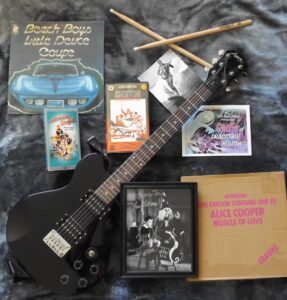 photo of rock memorabilia on a bed including autographed guitar and cds.